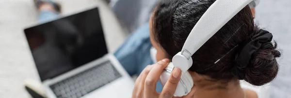 Top view of african american student wearing wireless headphones while listening audio book and using laptop, banner — Stock Photo