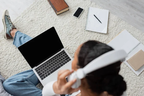 Top view of african american woman wearing wireless headphones while listening audio book and using laptop — Stock Photo