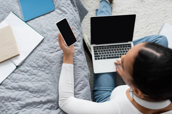 Top view of african american woman holding smartphone with blank screen near laptop while studying from home — Stock Photo