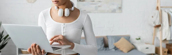 Cropped view of african american student with wireless headphones on neck using laptop in modern bedroom, banner — Stock Photo