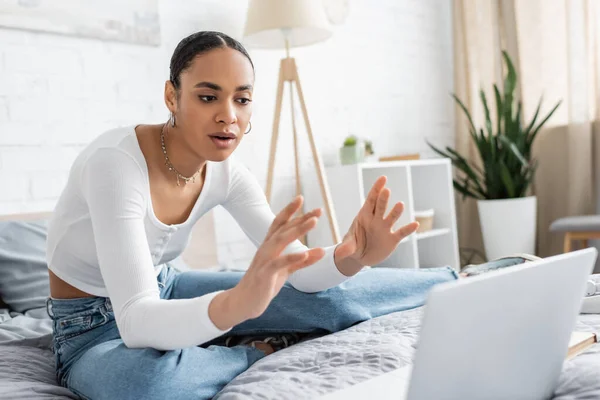 African american student talking during webinar on blurred laptop in bedroom — Stock Photo