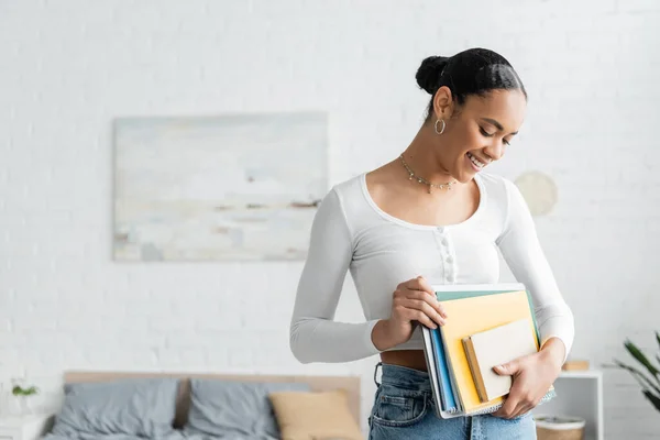 Positive afrikanisch-amerikanische Studentin schaut auf Notizbücher im Schlafzimmer — Stockfoto