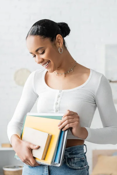 Alegre estudiante afroamericano mirando cuadernos en casa - foto de stock