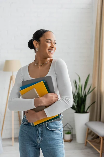 Alegre estudiante afroamericano sosteniendo cuadernos en casa - foto de stock