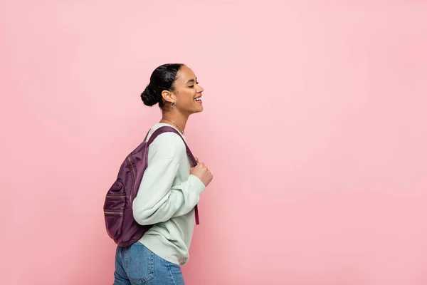 Estudiante afroamericano positivo con mochila de pie aislado en rosa - foto de stock