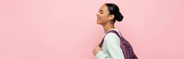 Cheerful african american student with backpack walking isolated on pink, banner — Stock Photo