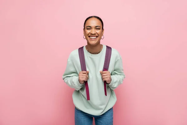 Усміхнений афроамериканський студент тримає рюкзак ізольований на рожевому — стокове фото