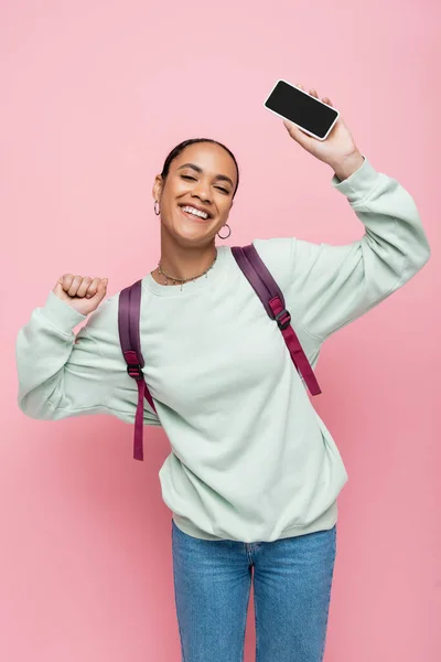 Positive afrikanisch-amerikanische Studentin in Sweatshirt und Jeans hält Handy mit leerem Bildschirm isoliert auf rosa — Stockfoto