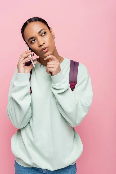 Offensiv afrikanisch-amerikanischer Student mit Rucksack spricht auf Smartphone isoliert auf rosa — Stockfoto