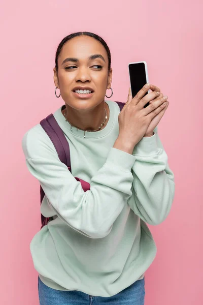 Estudiante afroamericano estresado cubriendo smartphone con mano aislada en rosa - foto de stock