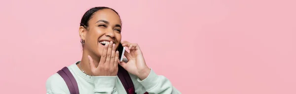 Estudiante afroamericano despreocupado hablando por teléfono celular aislado en rosa, pancarta - foto de stock