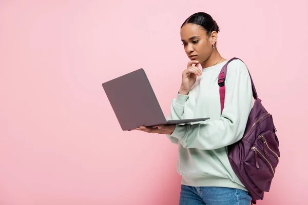 Estudante americano africano pensativo com mochila usando laptop em fundo rosa — Fotografia de Stock