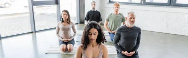 Gente multicultural meditando en Thunderbolt asana sobre esterillas de yoga en estudio, banner - foto de stock
