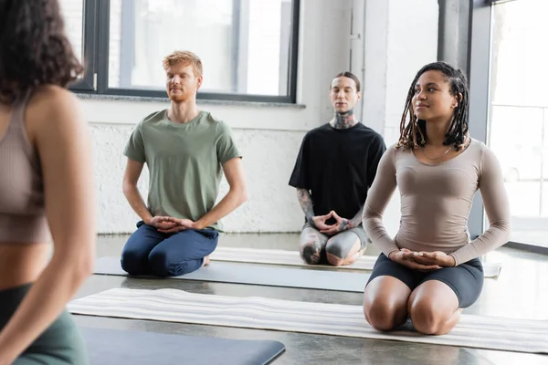 Sorridente donna afroamericana che medita a Thunderbolt asana in gruppo in classe di yoga — Stock Photo