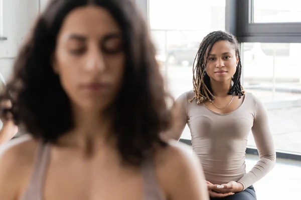 Jeune femme afro-américaine regardant la caméra près des personnes floues en cours de yoga — Photo de stock