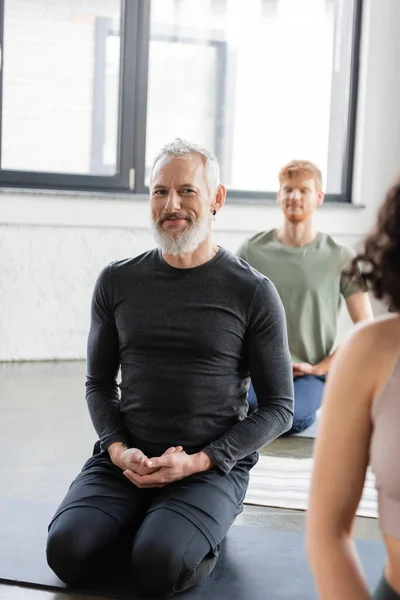 Улыбающийся мужчина средних лет смотрит в камеру, практикуя йогу в Thunderbolt asana в студии — стоковое фото