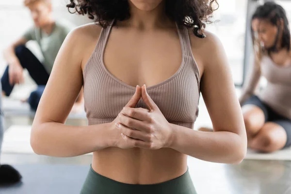 Vista recortada de la mujer meditando cerca de personas borrosas en clase de yoga - foto de stock