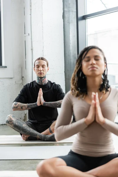 Jovem tatuado homem meditando e fazendo anjali mudra na aula de ioga — Fotografia de Stock