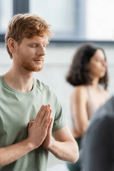 Redhead man with closed eyes doing anjali mudra in yoga class — Stock Photo