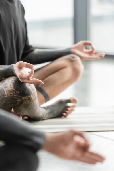 Vue recadrée de l'homme tatoué pratiquant mudra gyan en classe de yoga — Photo de stock