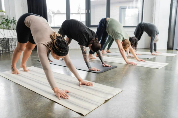 Young african american woman doing Downward Facing Dog asana in group in yoga class — Stock Photo