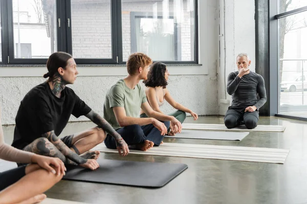 Coach montrant la technique de respiration narine au groupe interracial en cours de yoga — Photo de stock