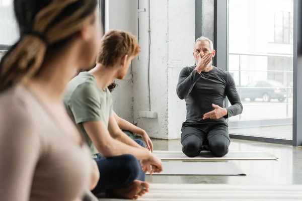 Middle aged coach explaining nostril breathing near blurred interracial group in yoga class — Stock Photo