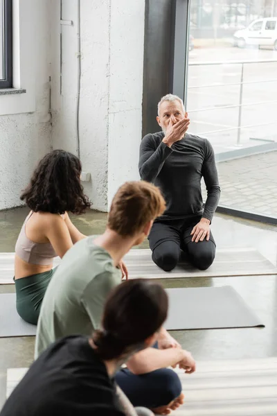 Mature coach showing nostril breathing to blurred group in yoga studio — Stock Photo