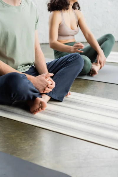 Cropped view of man sitting in fire log asana on mat in yoga class — Stock Photo