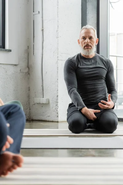 Middle aged coach talking near blurred people in yoga class — Stock Photo