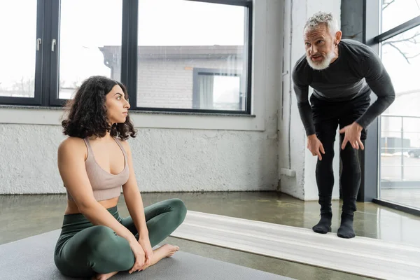 Reifer Trainer im Gespräch mit einer Frau aus dem Nahen Osten im Yoga-Studio — Stockfoto