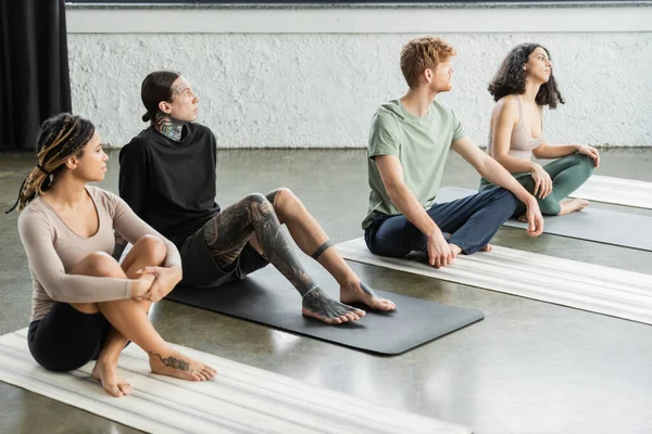 Young interracial people sitting on mats in yoga studio — Stock Photo