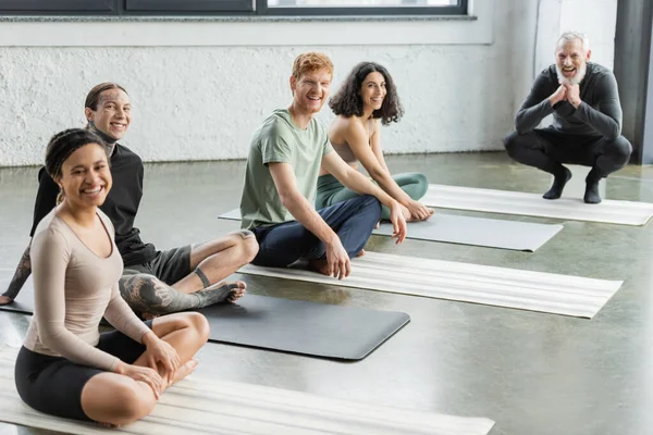 Groupe multiethnique joyeux et entraîneur regardant la caméra dans le studio de yoga — Photo de stock