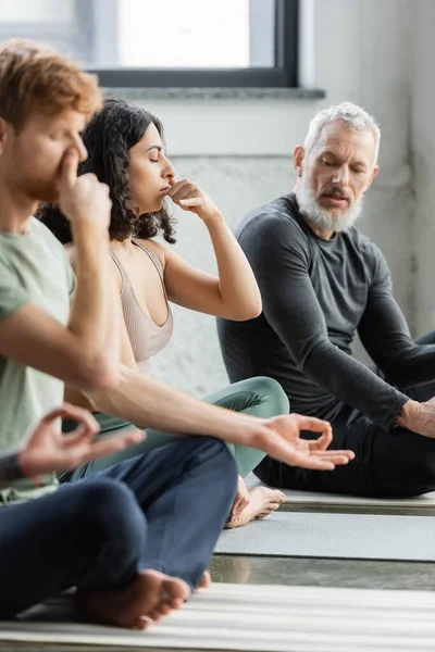 Middle eastern woman practicing nostril breathing near mature coach in yoga studio — Stock Photo