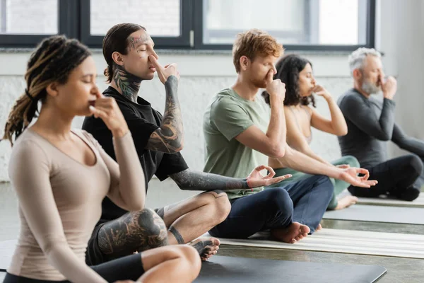 Tatuato uomo praticare la respirazione narice e mudra gyan in classe di yoga — Foto stock