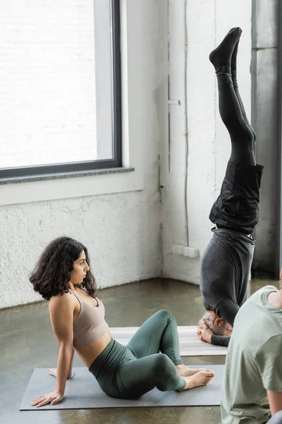 Nahöstliche Frau in Sportbekleidung sitzt auf Matte neben Leuten im Yoga-Kurs — Stockfoto