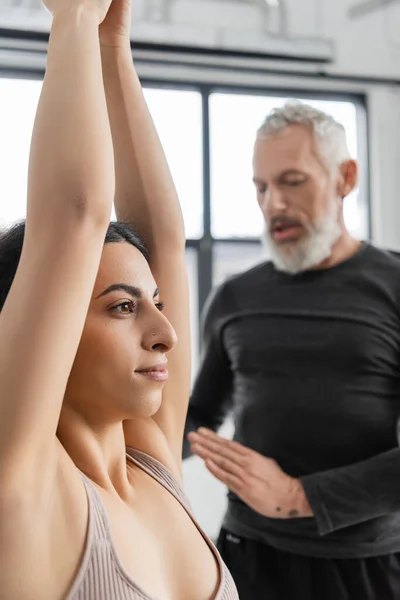 Женщина с Ближнего Востока практикует полумесяц Лунге Асана рядом с размытым тренером в классе йоги — стоковое фото
