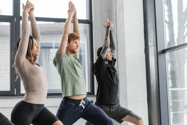 Jóvenes multiétnicos de pie en Crescent Lunge asana en clase de yoga - foto de stock