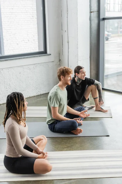 Молоді усміхнені багатоетнічні люди розмовляють на килимках у класі йоги — стокове фото