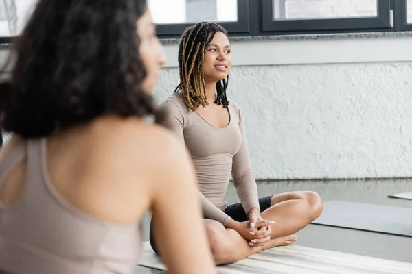 Femme afro-américaine souriante assise sur un tapis dans un studio de yoga — Photo de stock