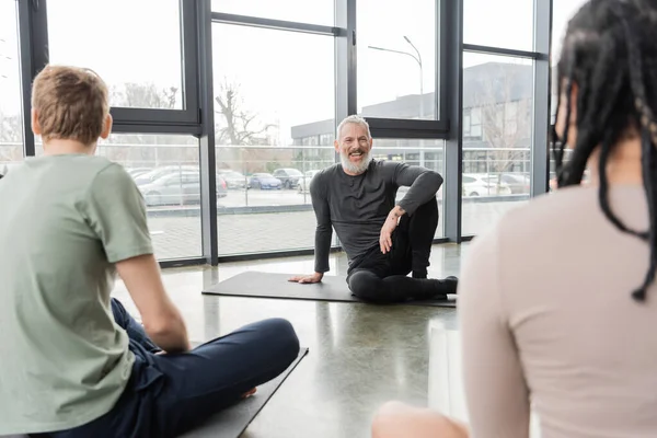 Treinador positivo olhando para pessoas multiétnicas desfocadas no estúdio de ioga — Fotografia de Stock