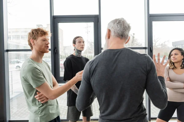 Ruiva homem falando com treinador maduro desfocado no estúdio de ioga — Fotografia de Stock