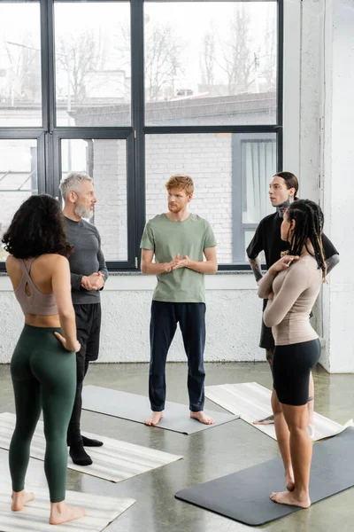 Міжрасові люди дивляться на зрілого тренера, стоячи на килимках в класі йоги — стокове фото