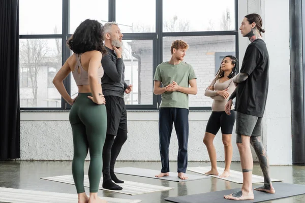 Багатоетнічні люди розмовляють, стоячи на килимках в студії йоги — стокове фото