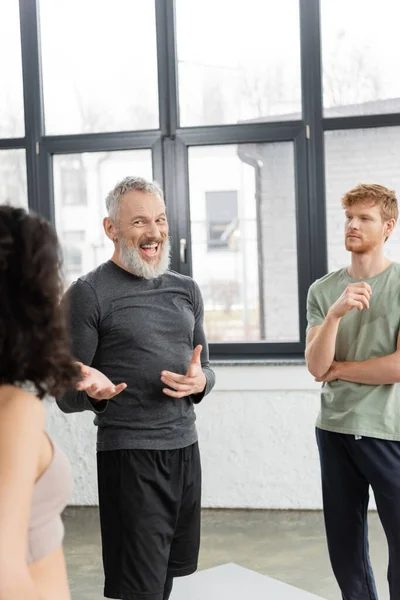 Positive mature coach pointing at blurred woman in yoga studio — Stock Photo
