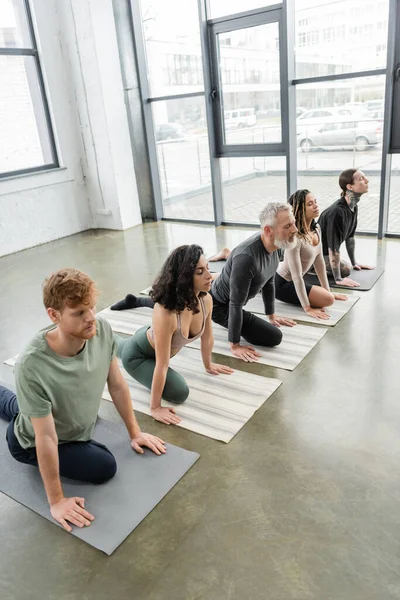 Grupo Interracial de personas practicando Media Paloma asana con los ojos cerrados en clase de yoga - foto de stock