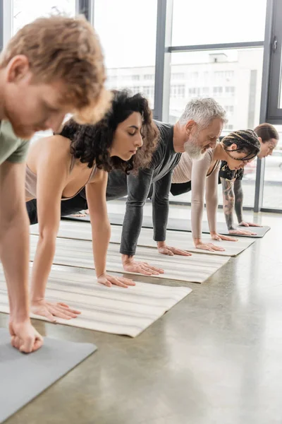 Personas multiétnicas de pie en Plank asana sobre esteras en clase de yoga - foto de stock