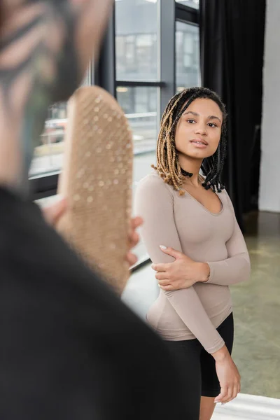 Joven mujer afroamericana mirando al hombre borroso con tablero de sadhu en estudio de yoga - foto de stock