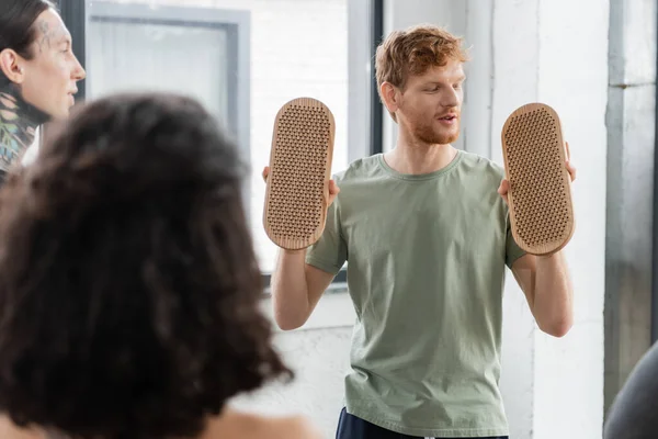 Young redhead man looking at sadhu board and talking to people in yoga class — Stock Photo