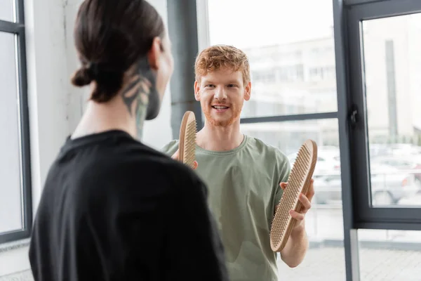 Smiling man holding sadhu board and talking to blurred friend in yoga studio — Stock Photo